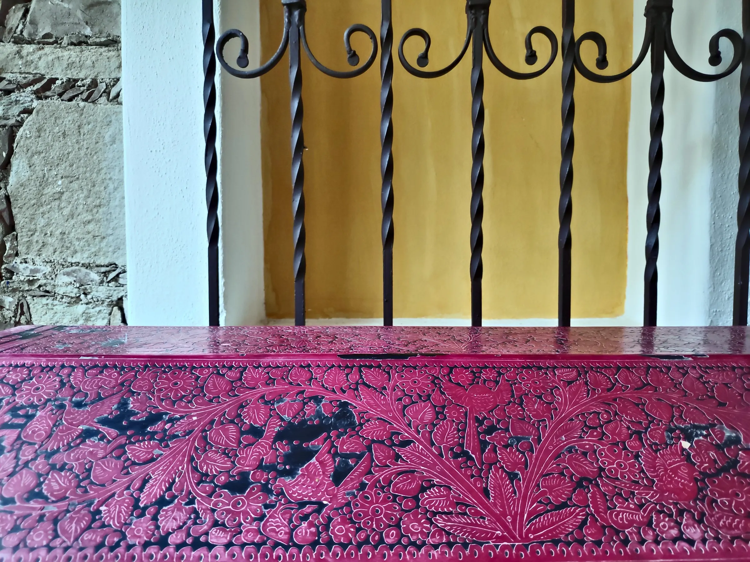 Red lacquered chest beneath a wrought-iron grille