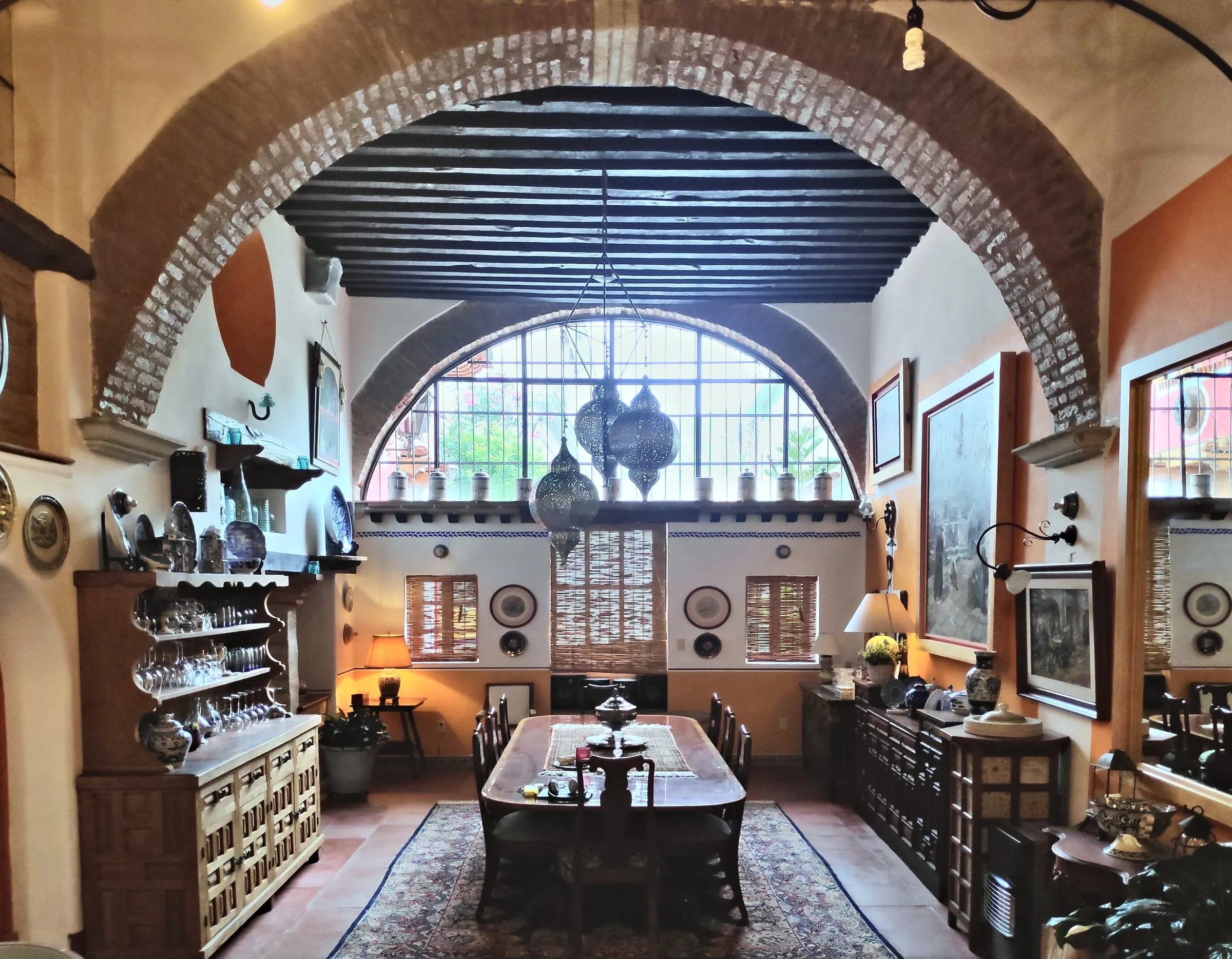 The grand dining room beneath a brick arch, with a half-moon window, blue beams and Moroccan lanterns
