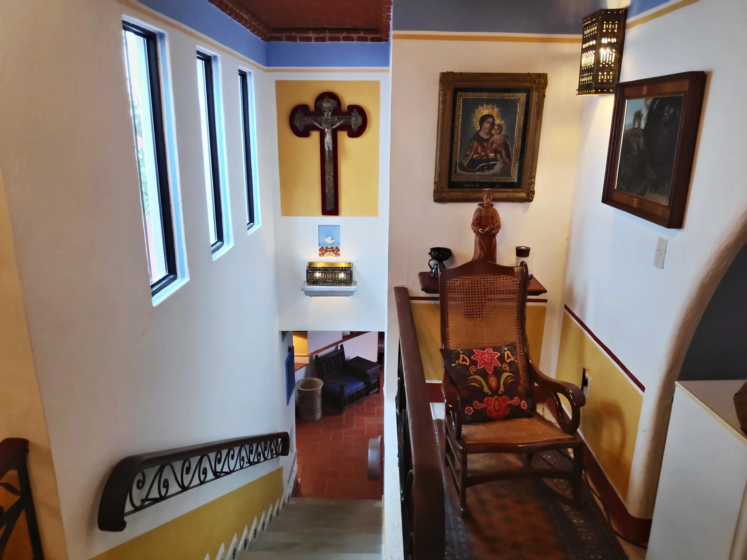 Staircase with a crucifix, religious paintings and a cane armchair with an embroidered cushion