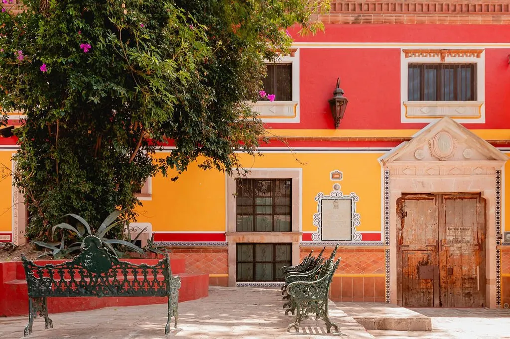 Red and yellow façade with a carved stone doorway and iron benches