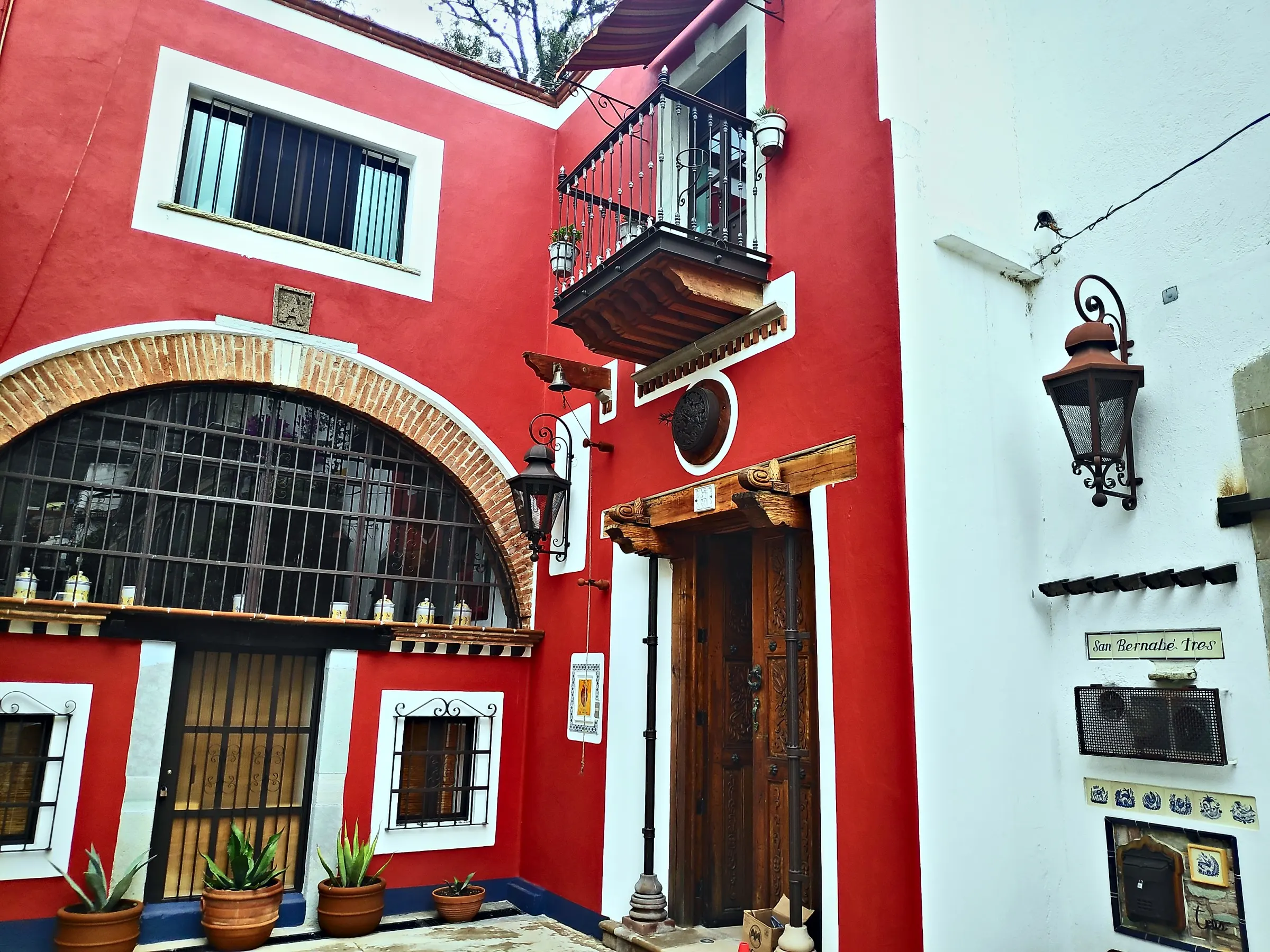 Entrance of Sanbernabé Tres: red mansion with an arched window, iron balcony, lanterns and the house sign
