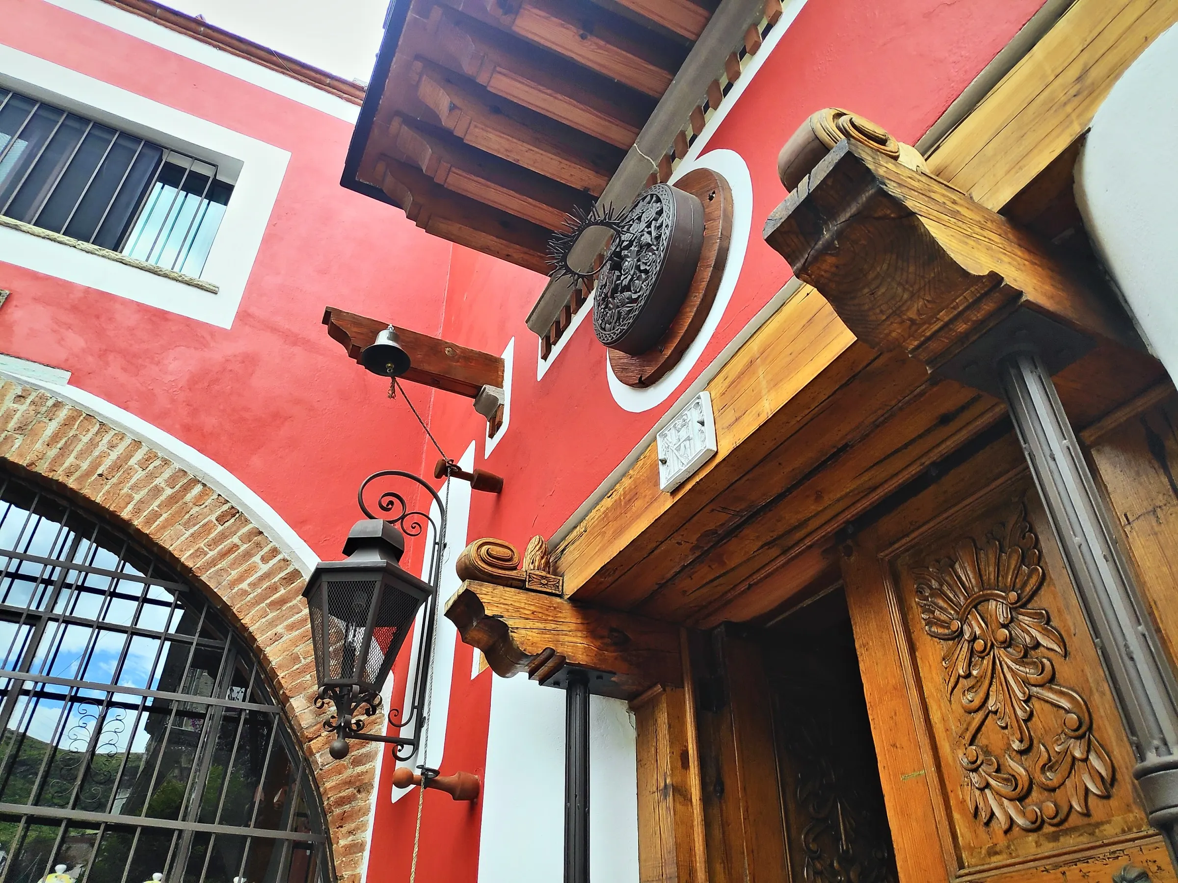 Carved wooden doorway, wrought-iron lantern and bell on the red façade