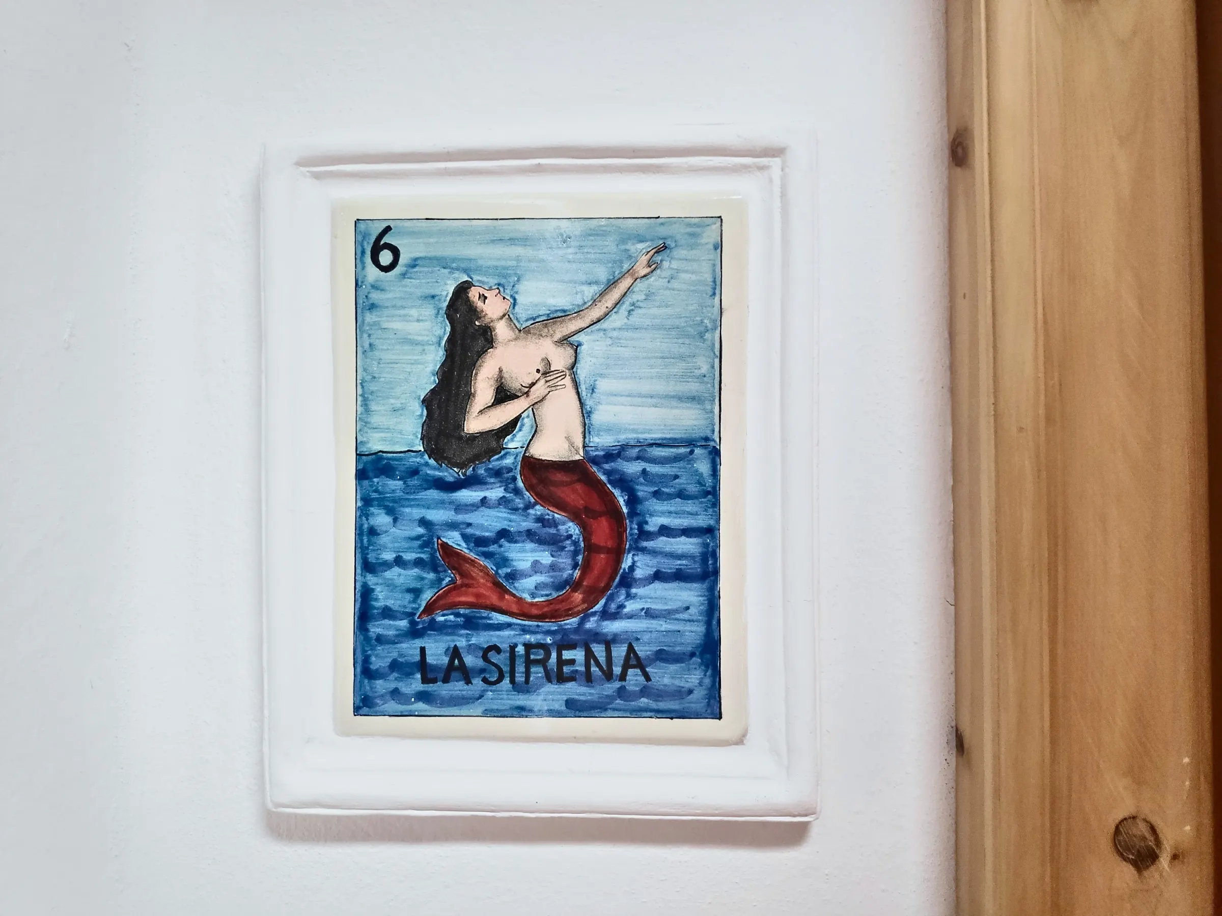 Lotería tile number 6, La Sirena, on the wall beside the suite door