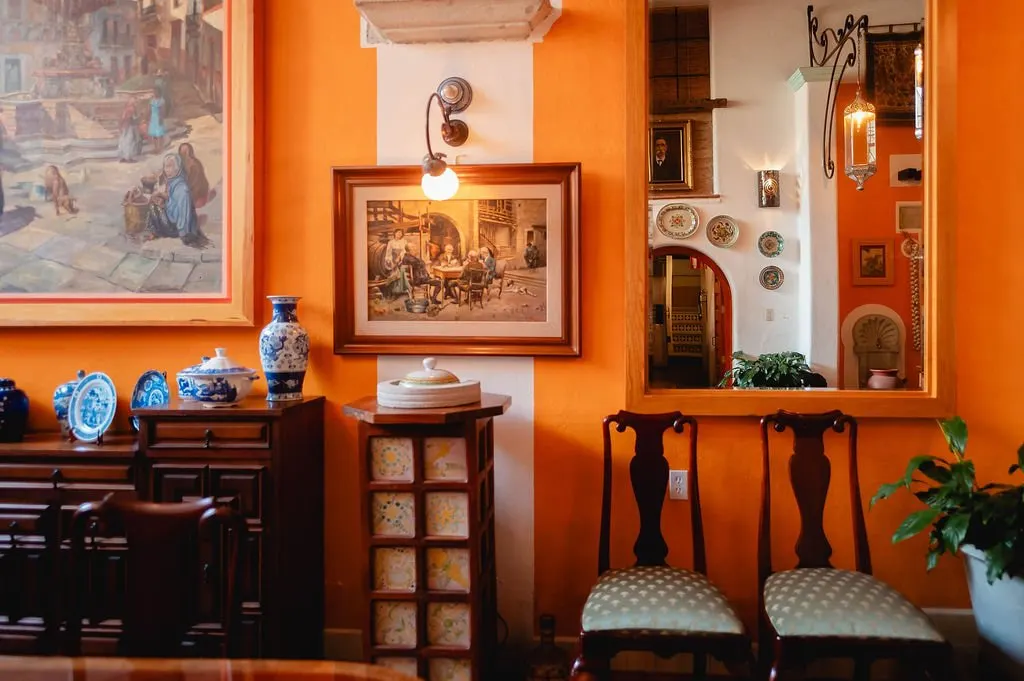 Orange wall with artwork, ceramics and antique chairs