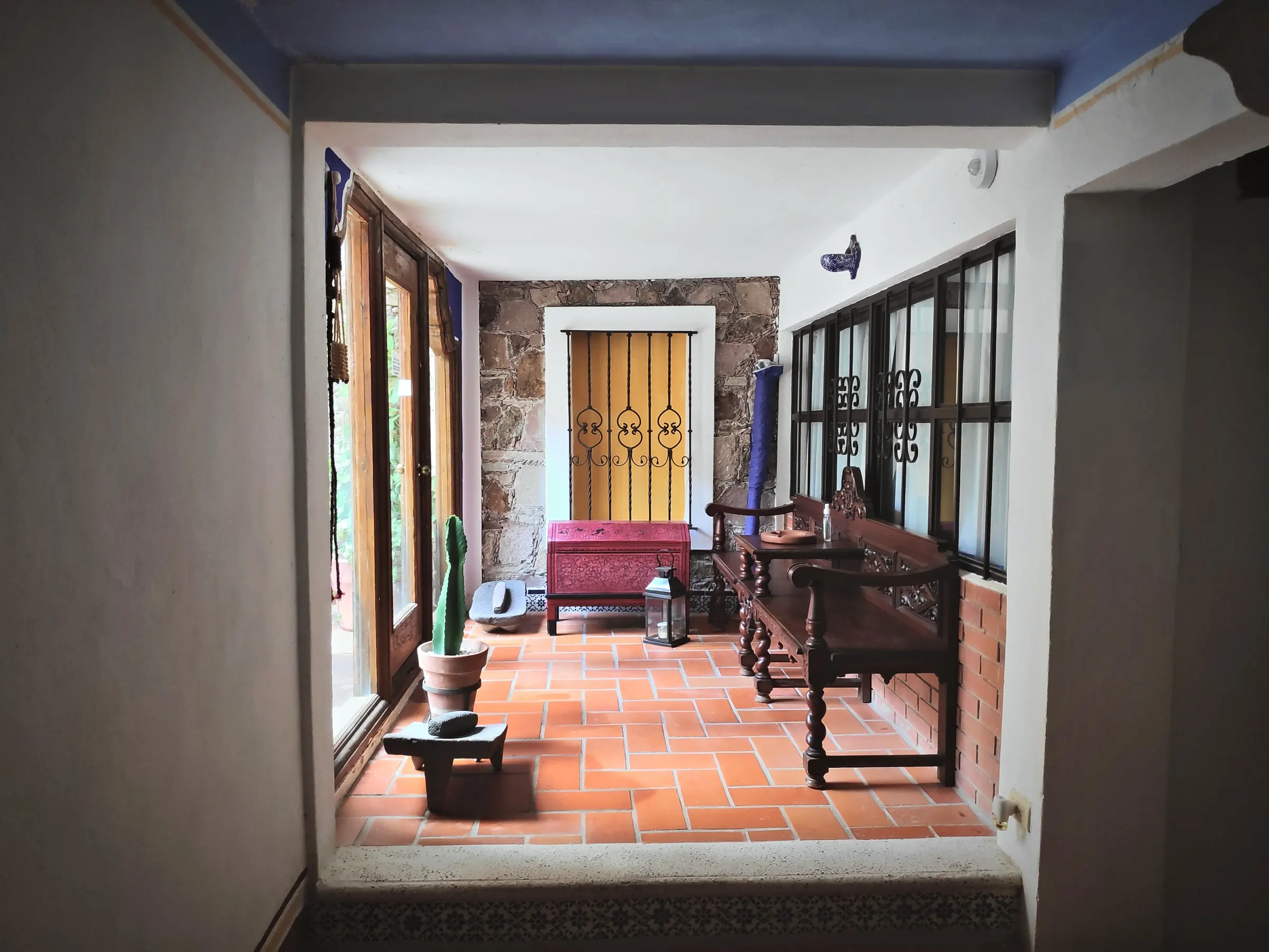 Terracotta corridor with wooden benches, a red chest and a yellow door at the end
