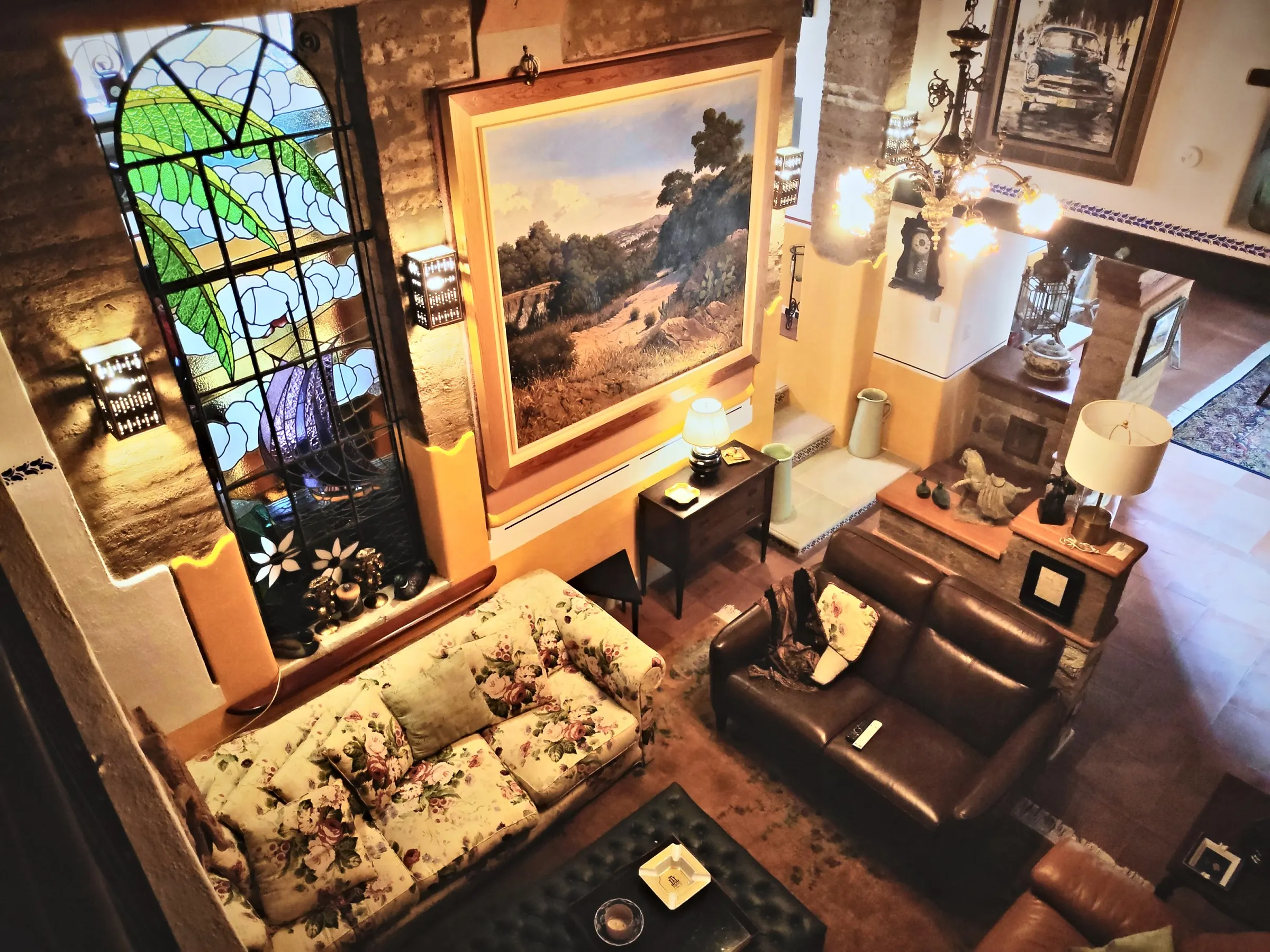 The living room seen from the mezzanine: stained glass, a large landscape painting, sofas and a lit chandelier