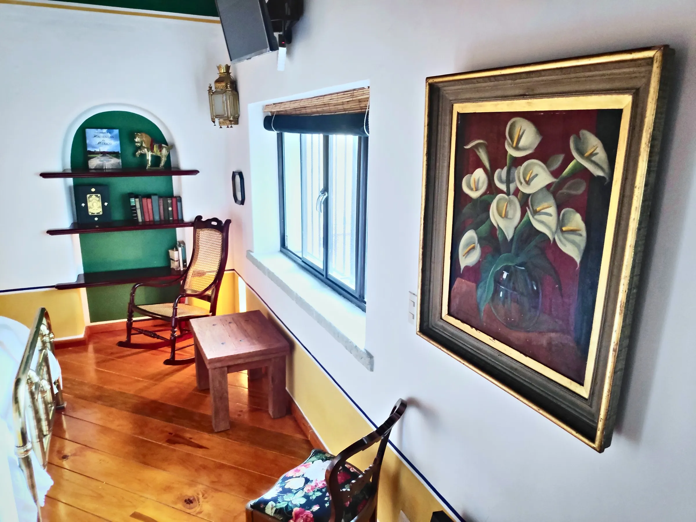 Reading corner in the Chichíndaro suite with a rocking chair, green niche bookshelf and calla lily painting