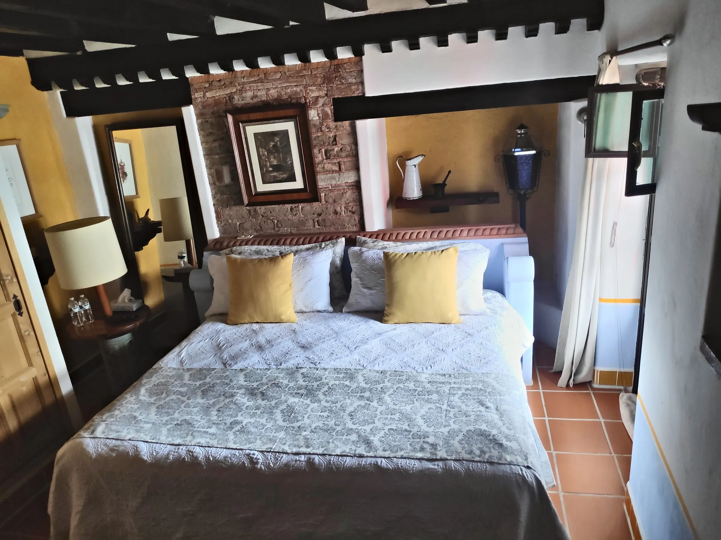 La Bolita suite: bed with marigold cushions beneath dark beams and a brick wall