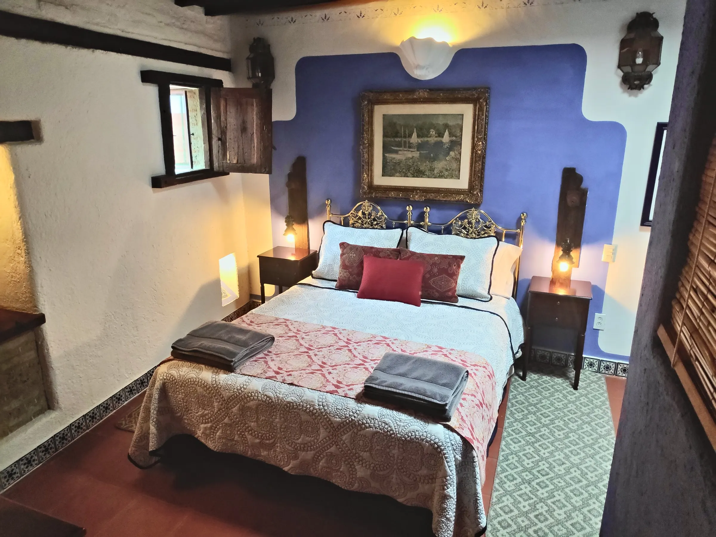 La Bufa suite: bed with a gilded wrought-iron headboard against the cobalt-blue wall, lamps lit