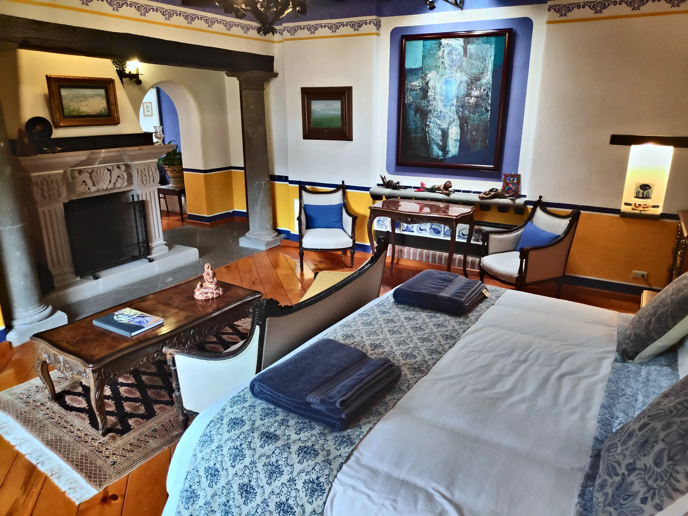 La Sirena suite: bed facing the carved stone fireplace, with a stone column and a large sea-toned painting